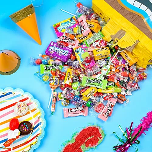 Assorted colorful candies spilled on a blue surface alongside party hats and decorations.