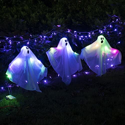 Three glowing ghost decorations with colorful lights in a garden setting.