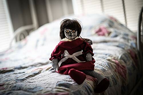 Creepy doll with dark hair and red dress on bed.