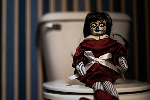 Creepy doll with dark hair and striped limbs sitting on a toilet lid.