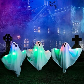 Three glowing ghost figures in front of a haunted house at night.