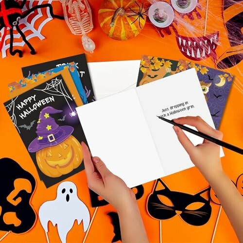 Person writing a Halloween card surrounded by decorations.