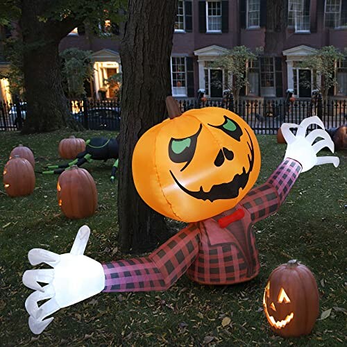 Inflatable pumpkin decoration with spooky face and glowing hands on a lawn with carved pumpkins.