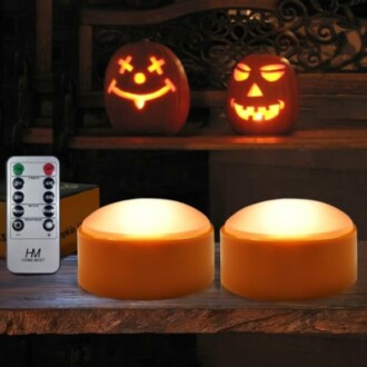 Two glowing pumpkins and LED candles with remote control on a table.