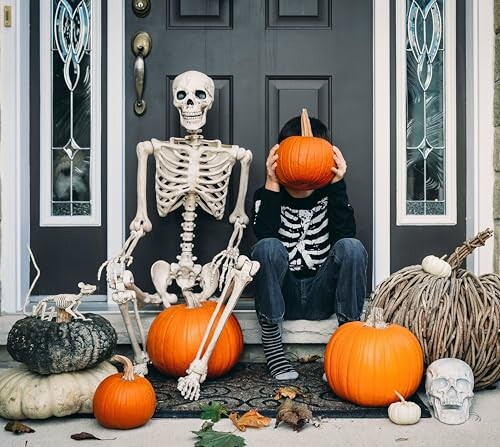 Child in skeleton costume with pumpkins and skeleton decoration on doorstep.