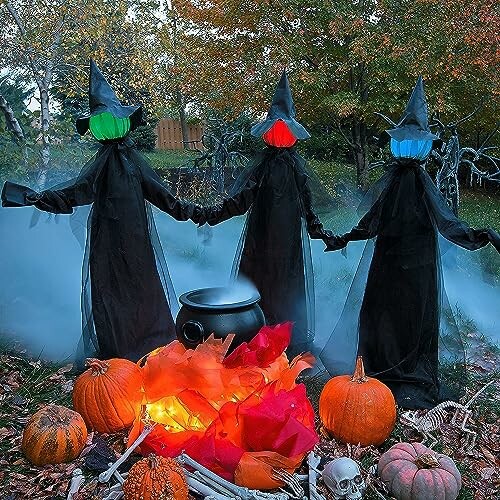 Three witch figures with colored face coverings holding hands around a cauldron with pumpkins and a skull in a spooky outdoor setting.