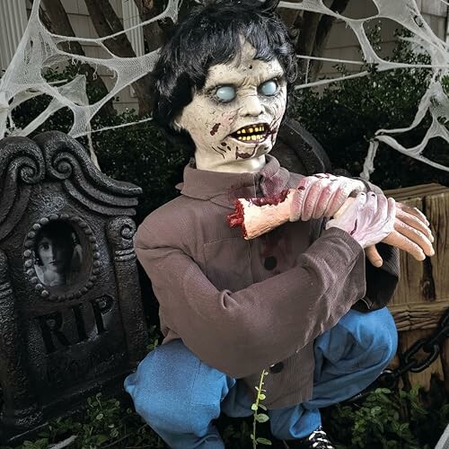 Creepy zombie decoration with severed arm and gravestone for Halloween.