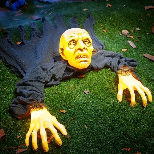 Halloween zombie decoration with a creepy face and hands on grass.