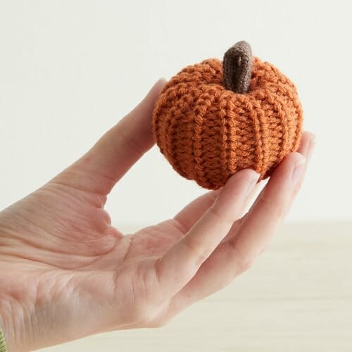 A hand holding a small crochet pumpkin.