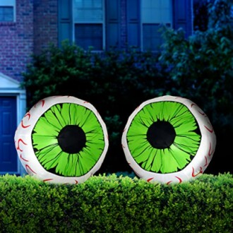 Two inflatable green eyeballs on a hedge in front of a house.