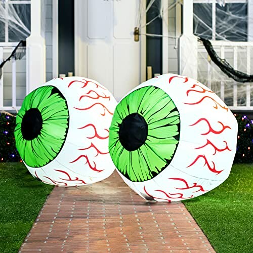 Two large inflatable eyeballs with green irises and red veins on a walkway.