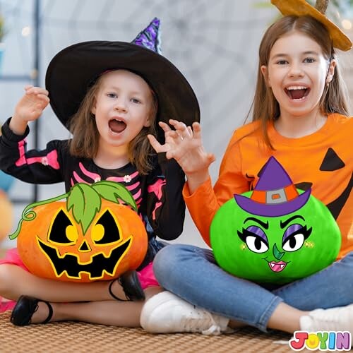 Two children in Halloween costumes holding decorated pumpkins.